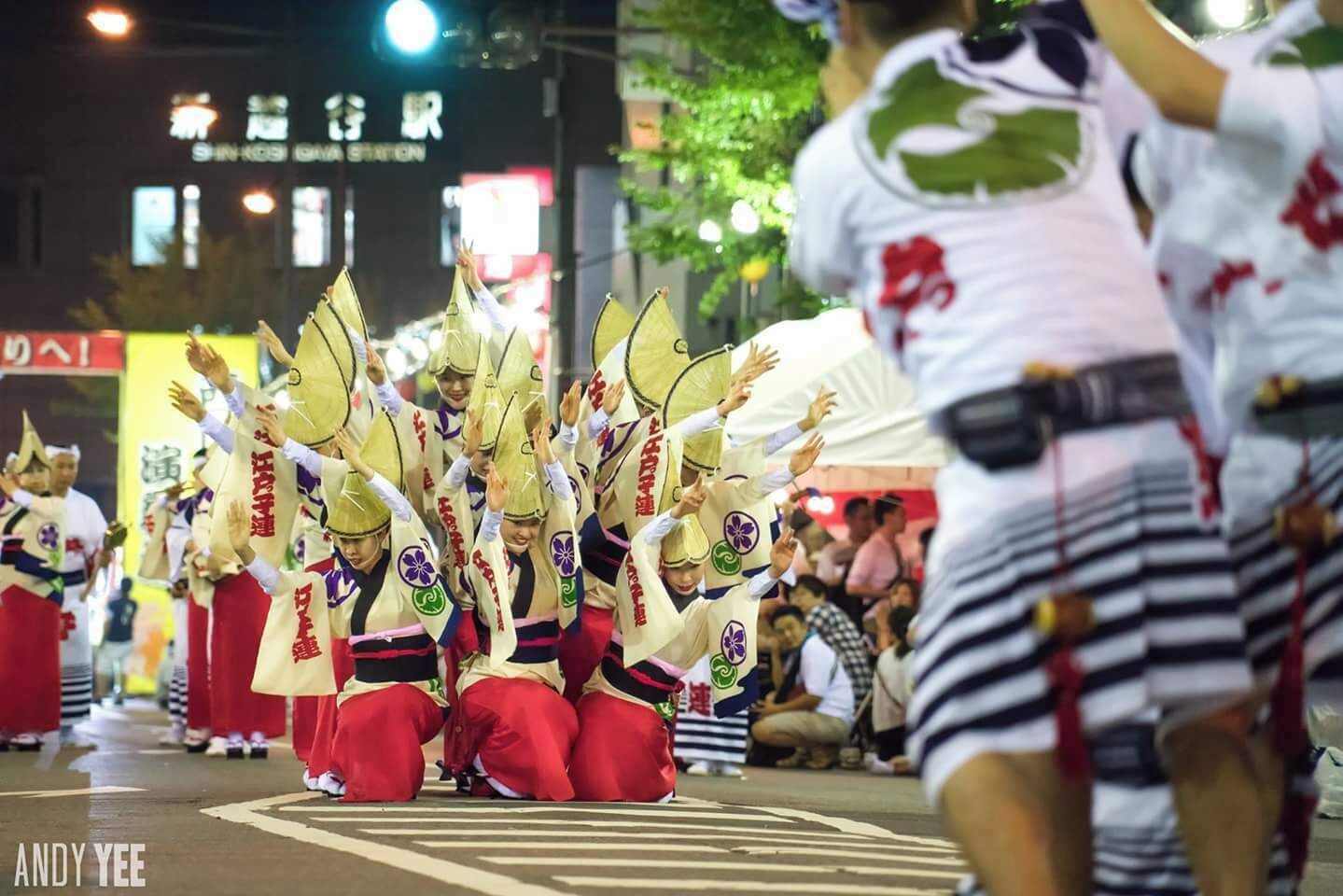 A group of performers in traditional attire with conical hats, performing on a street at night.