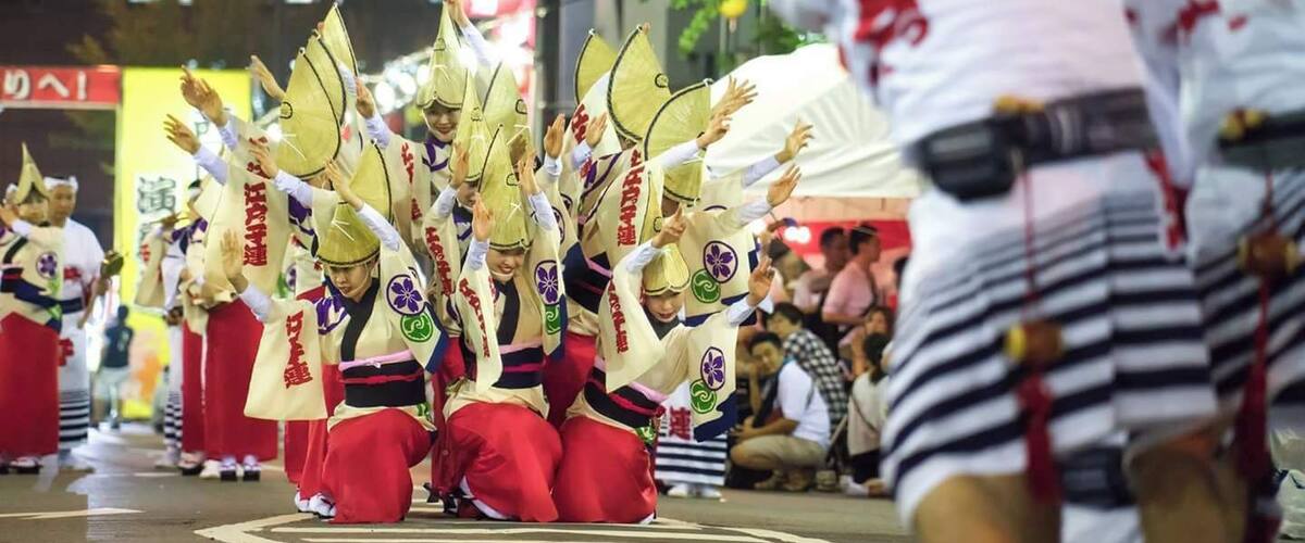 A group of performers in traditional attire with conical hats, performing on a street at night.