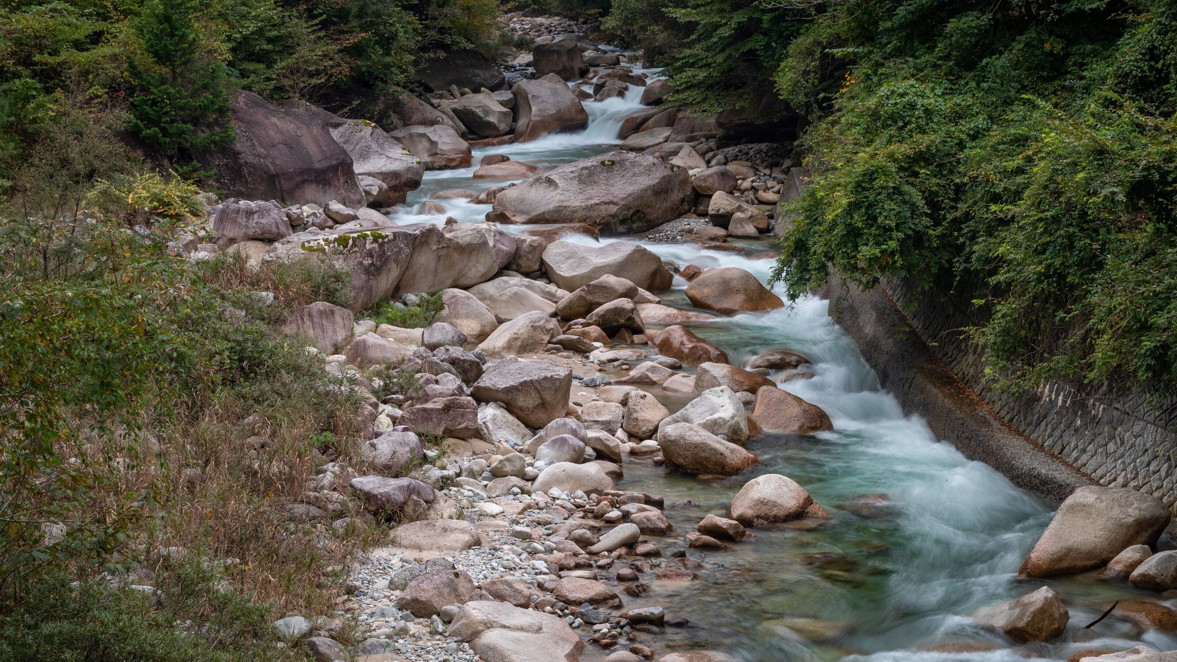 A river flowing through a rocky gorge with large boulders and dense green foliage.
