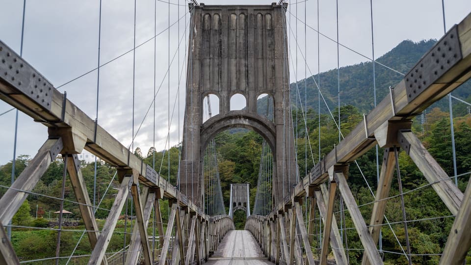 A wooden suspension bridge with a central arch and multiple cables.