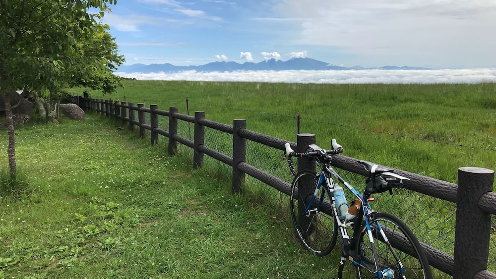 A bicycle parked by a wooden fence in a grassy field with mountains in the background.