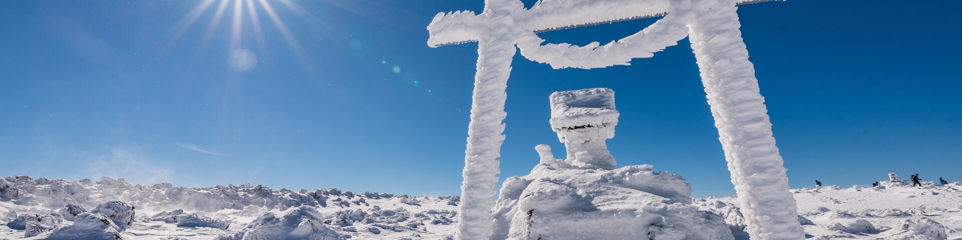 Un torii cubierto de nieve en un paisaje nevado, con el sol brillando intensamente en el cielo.