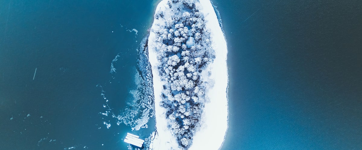 Aerial view of a snow covered island with forest surrounded by the deep blue waters of Lake Nojiri, Shinano, Nagano, Japan.