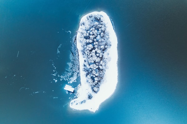 Aerial view of a snow covered island with forest surrounded by the deep blue waters of Lake Nojiri, Shinano, Nagano, Japan.