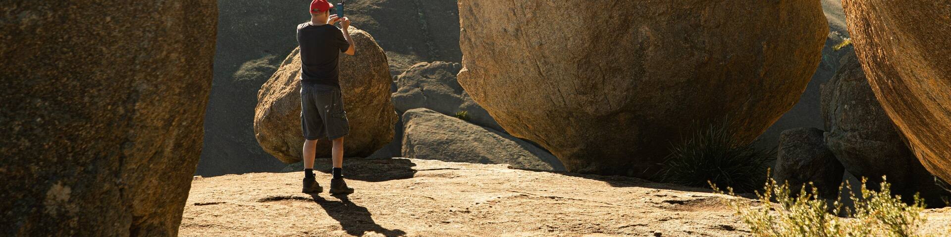 A person taking a photo with a smartphone in a rocky landscape with large boulders.