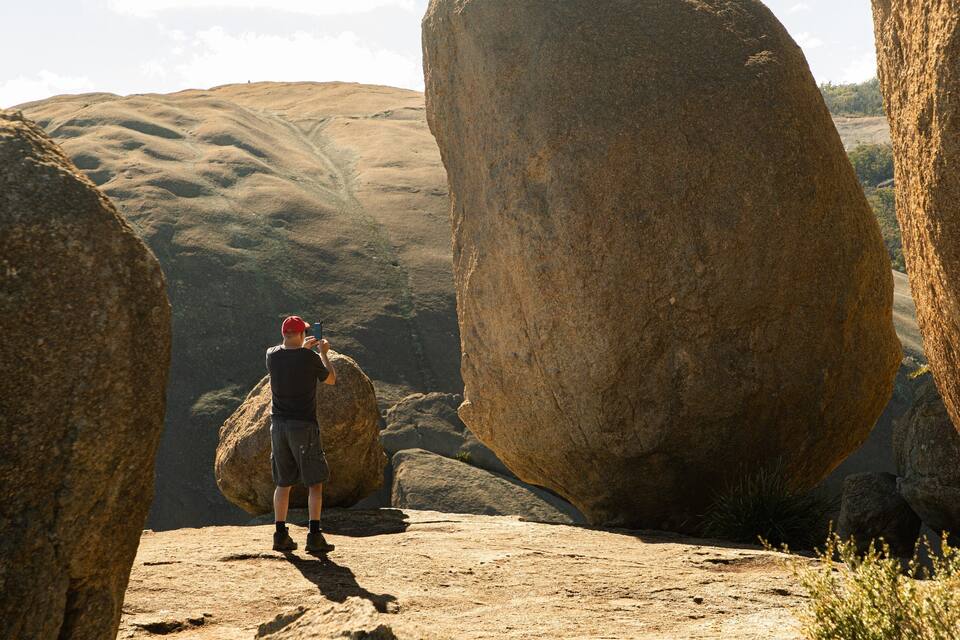 A person taking a photo with a smartphone in a rocky landscape with large boulders.