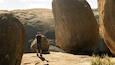 A person taking a photo with a smartphone in a rocky landscape with large boulders.