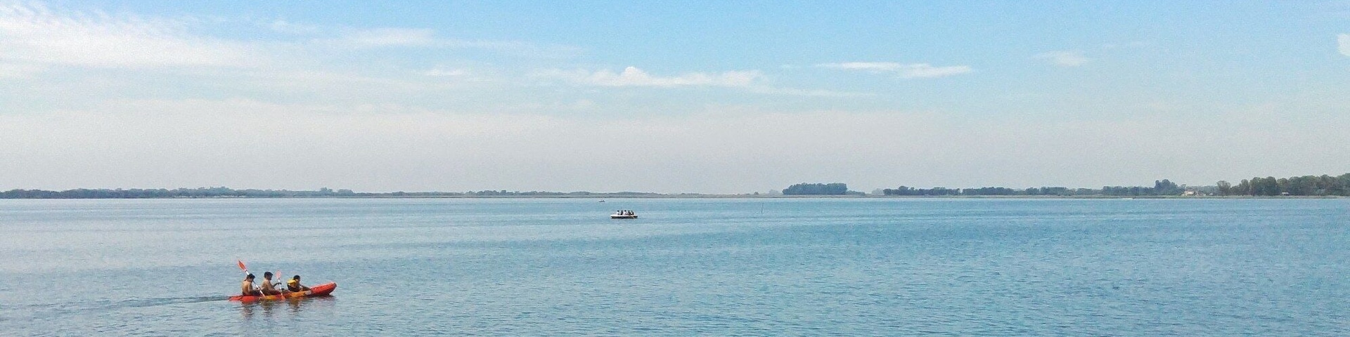 A calm body of water with kayaks and a distant boat.