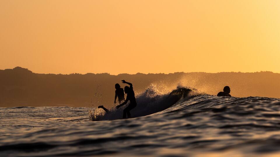 Surfers riding a wave at sunset with a distant shoreline.