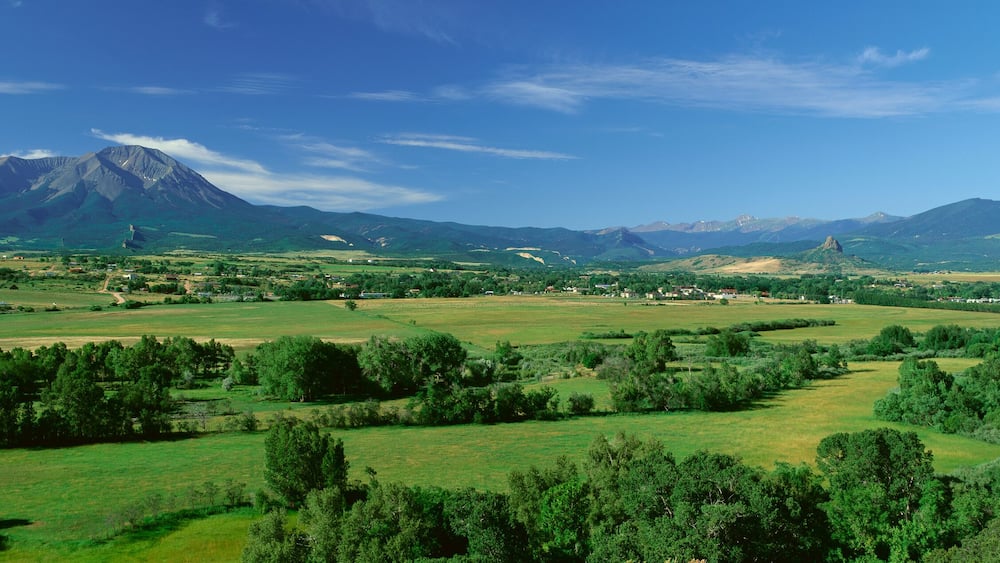 A mountainous landscape with a prominent peak, rolling green fields, and scattered trees.