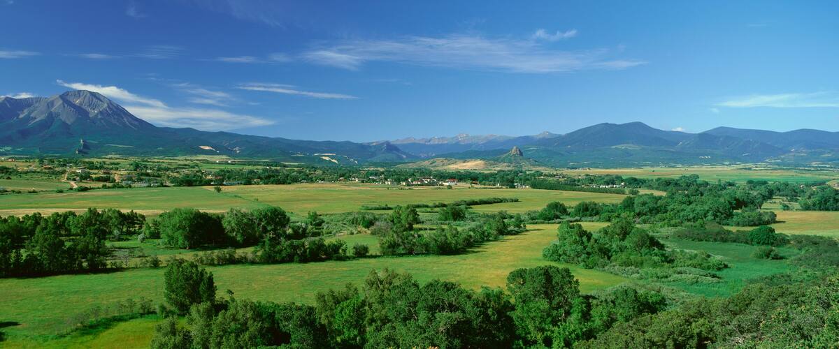 A mountainous landscape with a prominent peak, rolling green fields, and scattered trees.