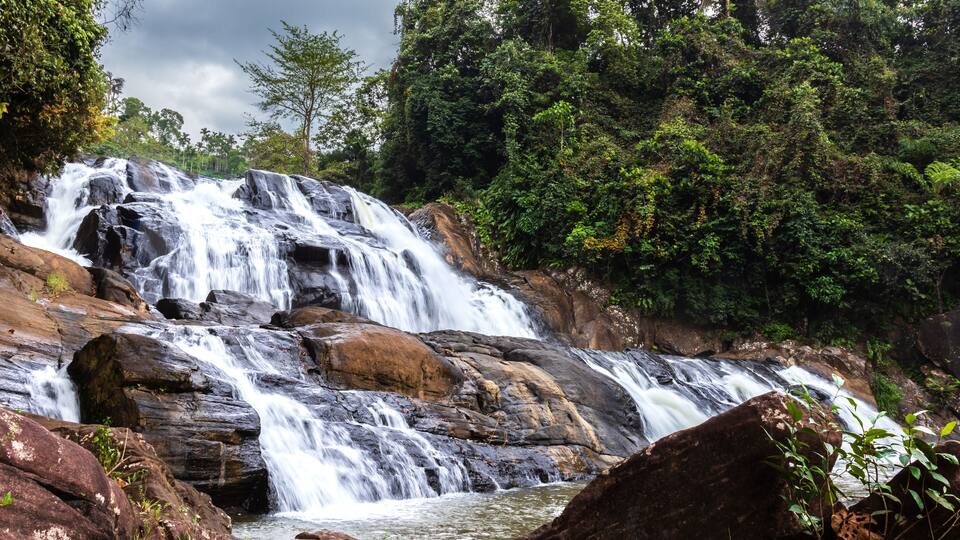 A multi-tiered waterfall surrounded by dense forest.
