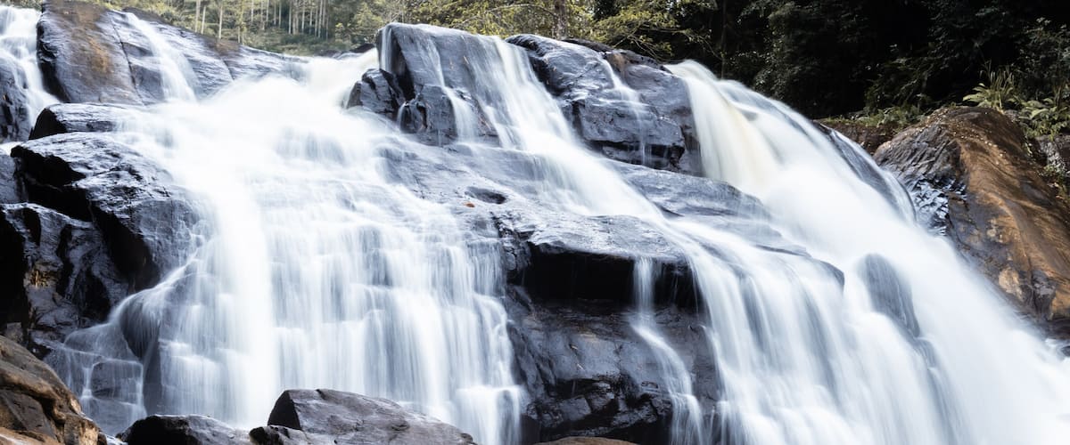 A multi-tiered waterfall cascading over large rocks in a forested area.