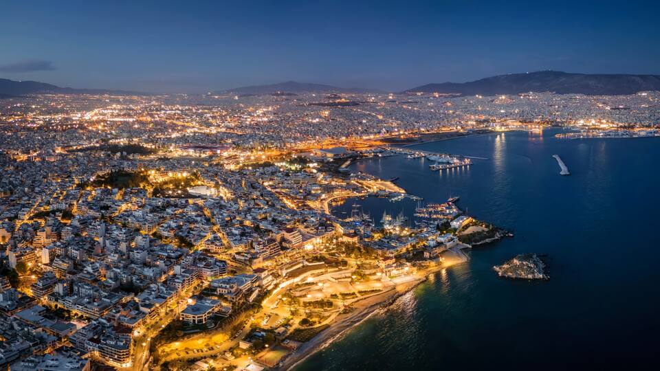 Aerial night view over the illuminated skyline of Piraeus, Athens, Greece, with Kstella Hill, Mikrolimano marina until the Faliro district