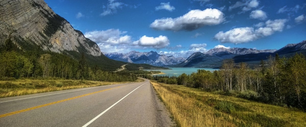A road leading through a mountainous landscape with a lake and a clear sky.