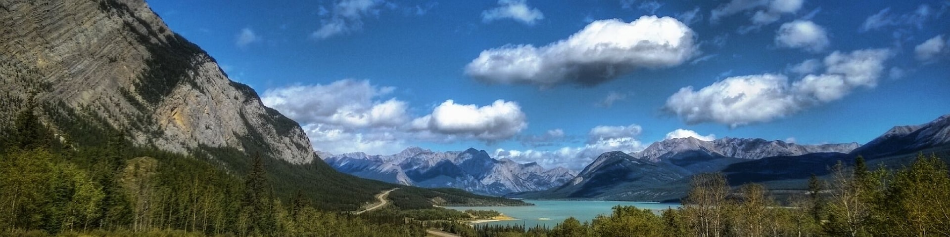 Uma estrada serpenteando por uma paisagem montanhosa com um lago e céu claro.