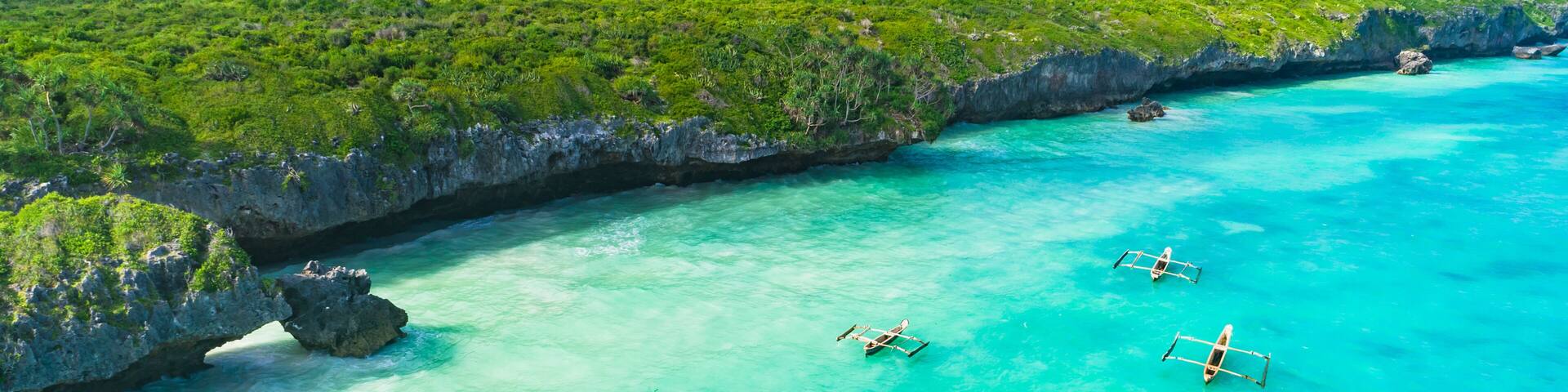 A turquoise sea with boats, a rocky coastline, and lush greenery.