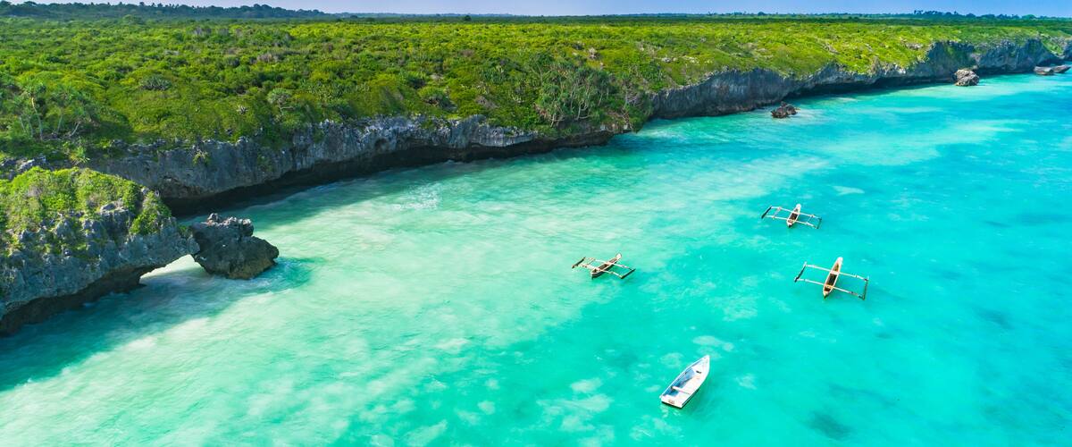 A turquoise sea with boats, a rocky coastline, and lush greenery.