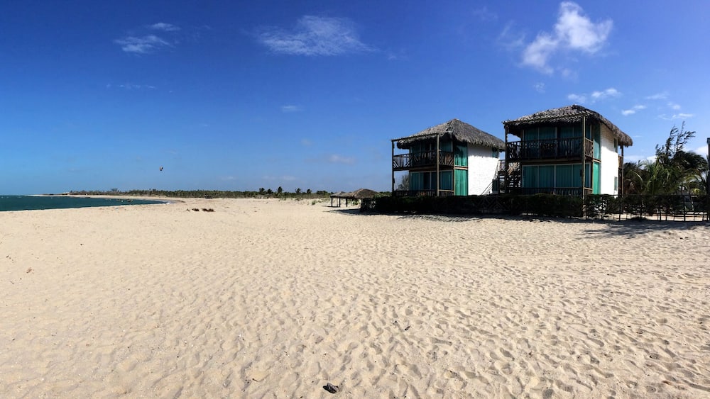 A sandy beach with a thatched-roof building and a clear blue sky.
