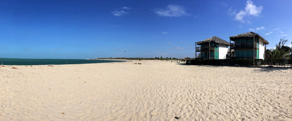 A sandy beach with a thatched-roof building and a clear blue sky.