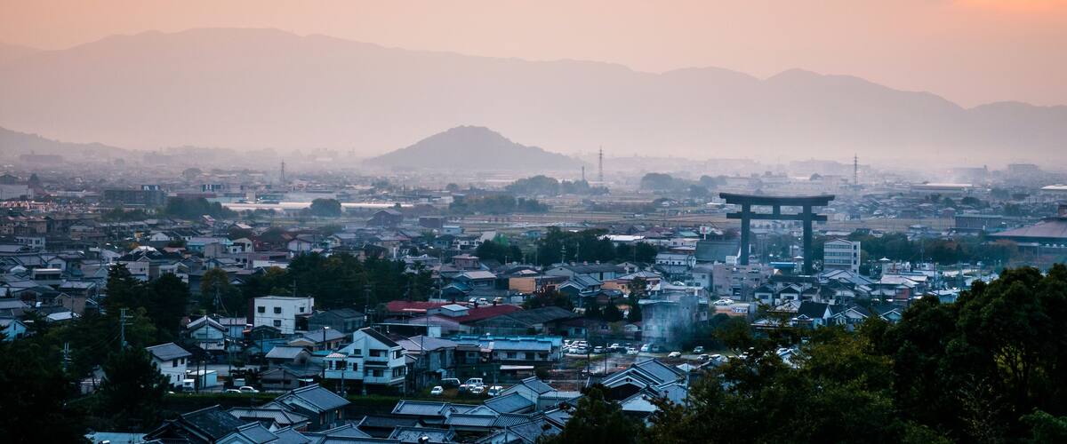 A cityscape with a prominent torii gate, surrounded by residential buildings and mountains in the background.