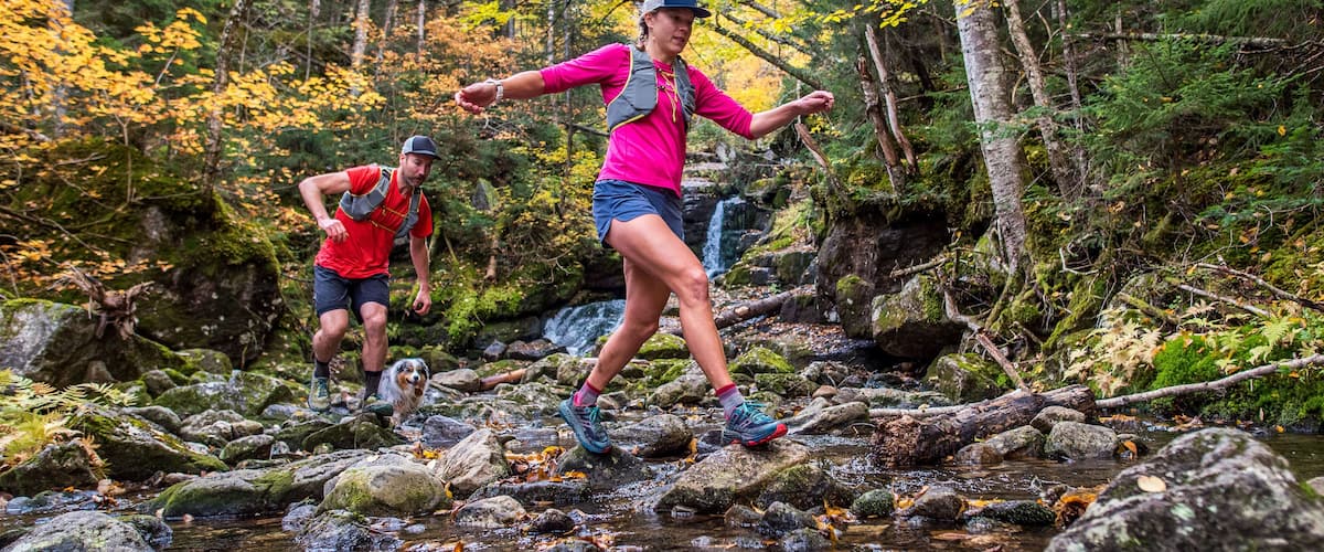 Two people hiking on a rocky stream surrounded by autumn-colored trees.
