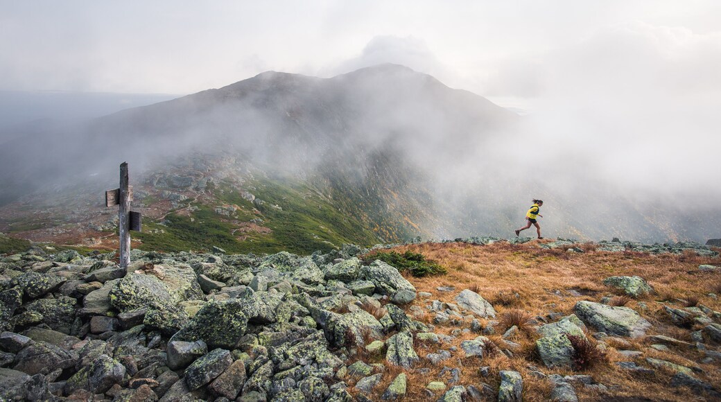 Woman running on ridge in clouds with mountains behind