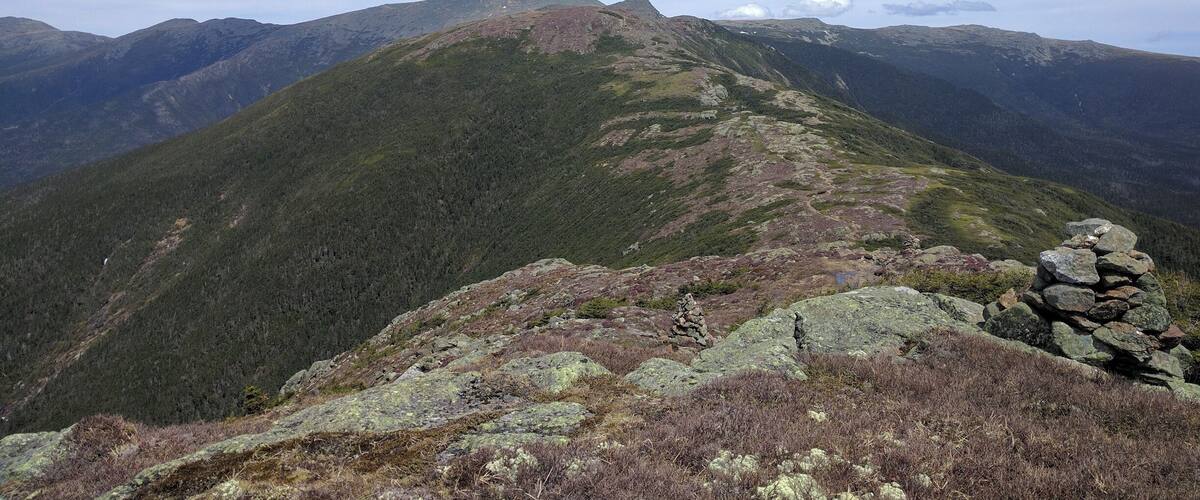 A mountain landscape with a clear sky, rocky terrain, and sparse vegetation.