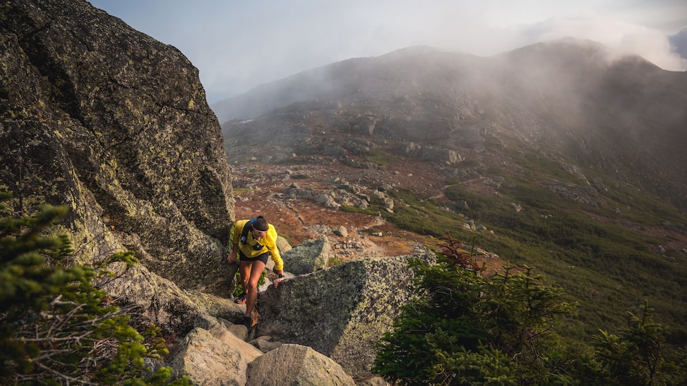 Woman scrambling in rocks on trail run with mountains behind
