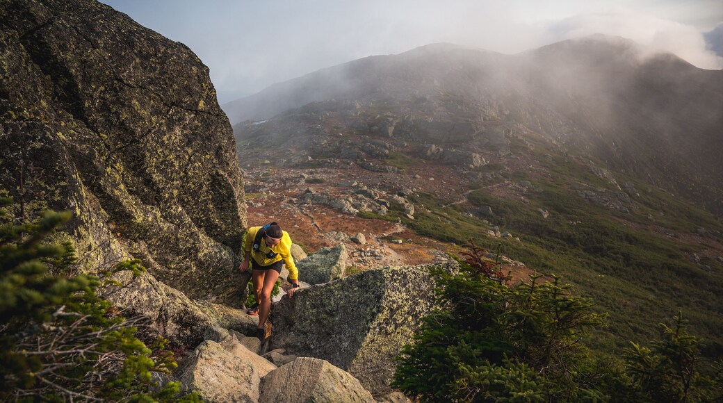 Woman scrambling in rocks on trail run with mountains behind
