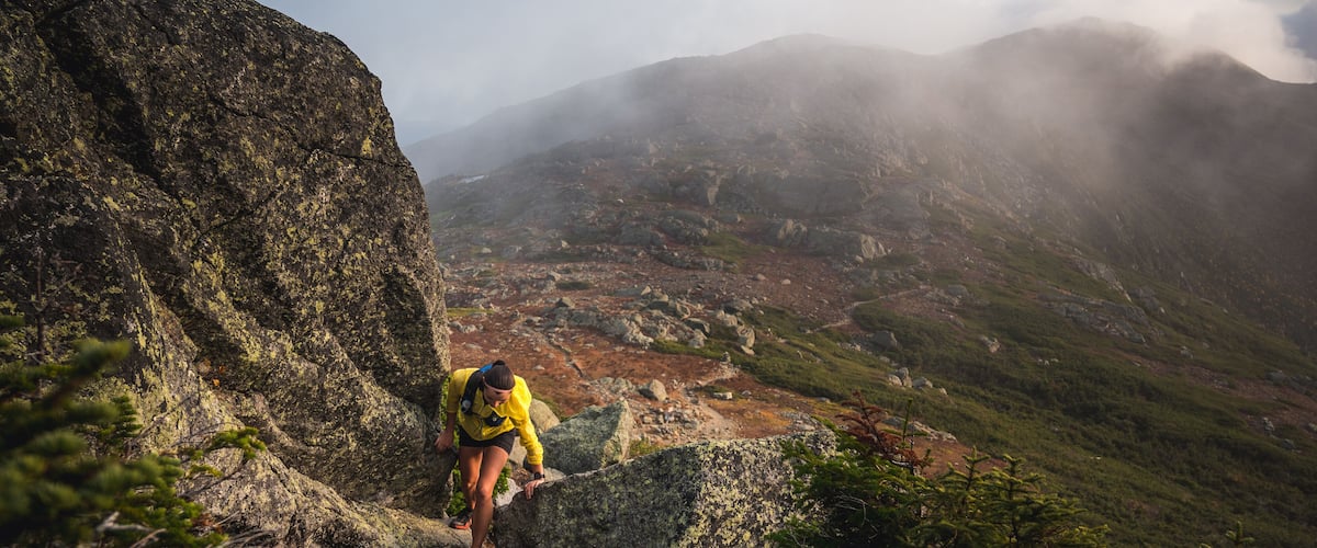 Woman scrambling in rocks on trail run with mountains behind