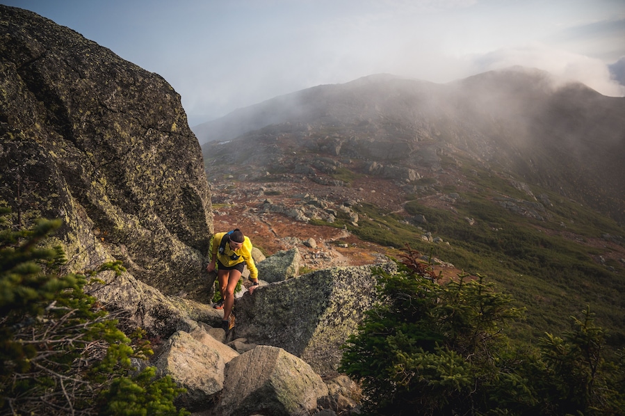 Woman scrambling in rocks on trail run with mountains behind