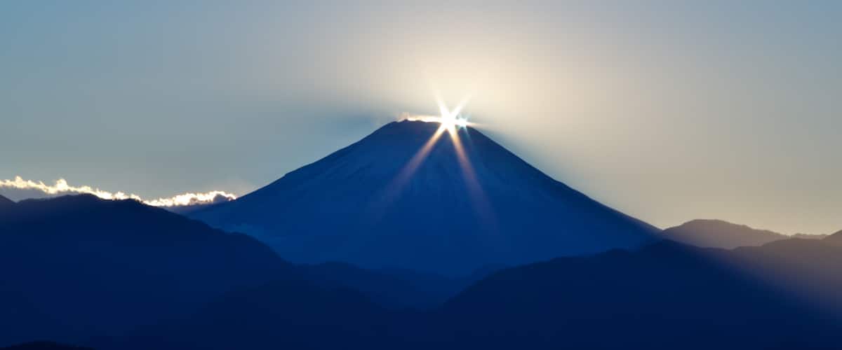 A mountain with a bright sun shining from behind it.