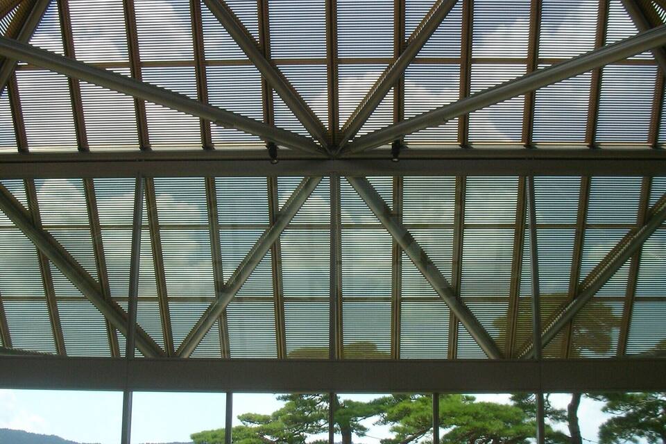A large glass-paneled structure with a metal framework, overlooking a mountainous landscape with trees.