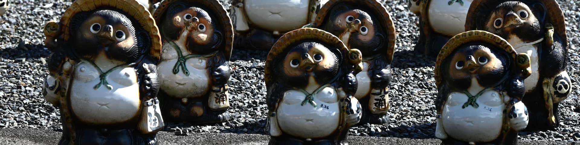 A collection of ceramic penguins with hats, arranged in rows on a gravel surface.