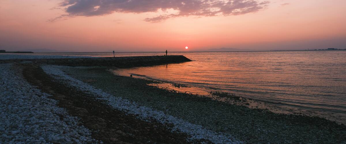 A sunset over a rocky shoreline with a pier extending into the water.