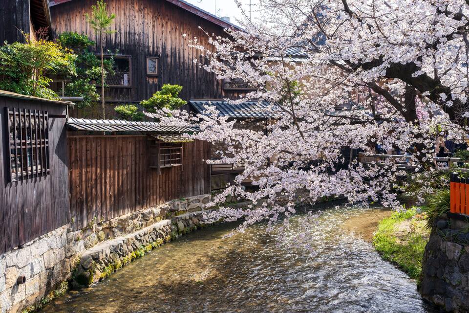 A traditional wooden building with a stone wall and a narrow water channel.