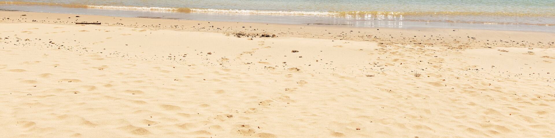 A sandy beach with clear turquoise water, two rocky outcrops, and a clear sky.