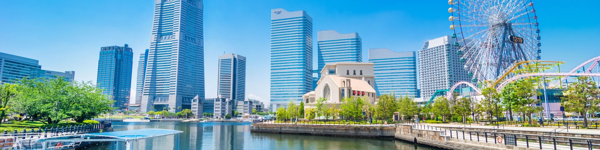 A cityscape with modern skyscrapers, a large Ferris wheel, and a river with a boat dock.