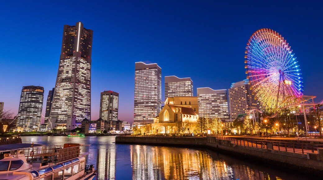 A city skyline with illuminated skyscrapers and a colorful Ferris wheel reflecting on the water.