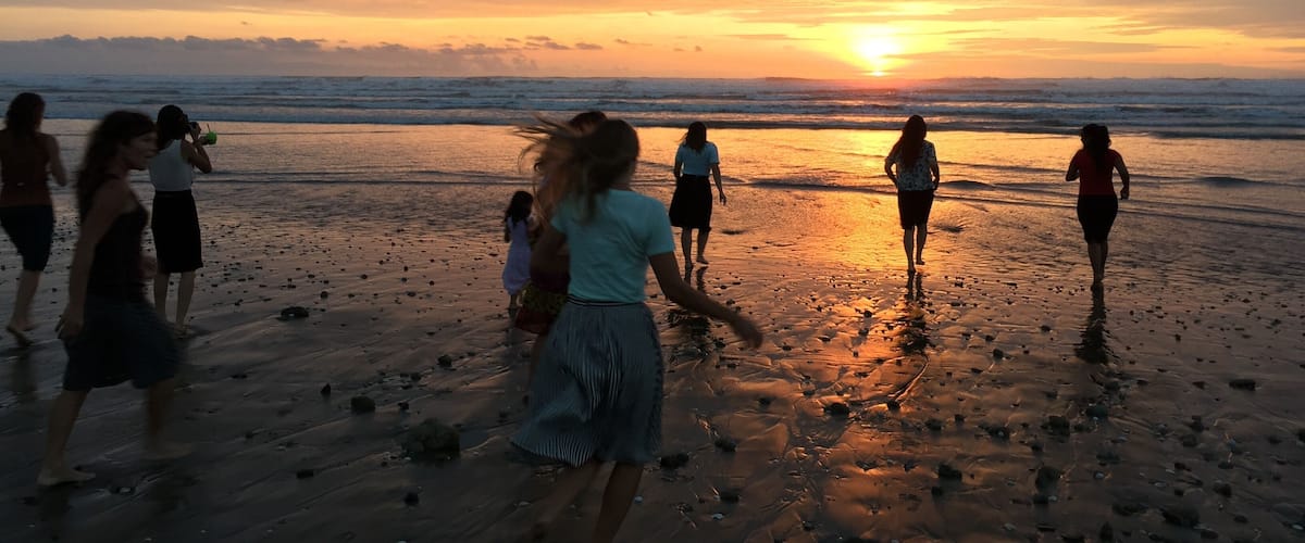 A sunset at the beach with people walking and a child playing.