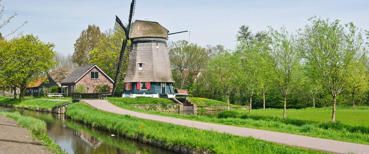 A traditional windmill, a canal, and a grassy area with trees and a pathway.