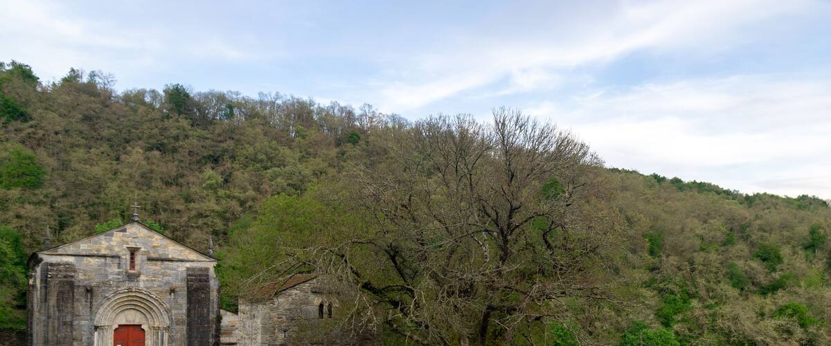 A stone church with a red door, surrounded by lush green grass and trees on a hillside.