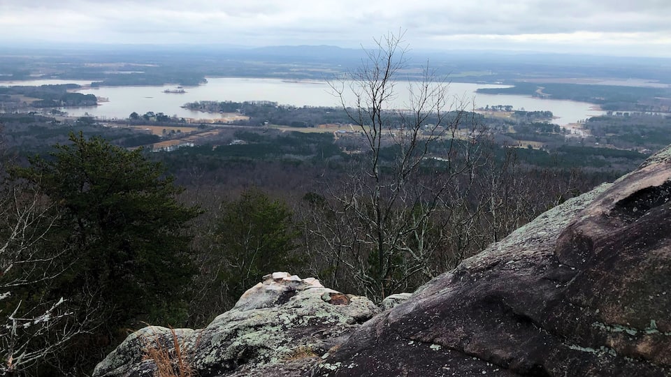 A mountainous landscape with a lake, forested areas, and rocky outcrops.