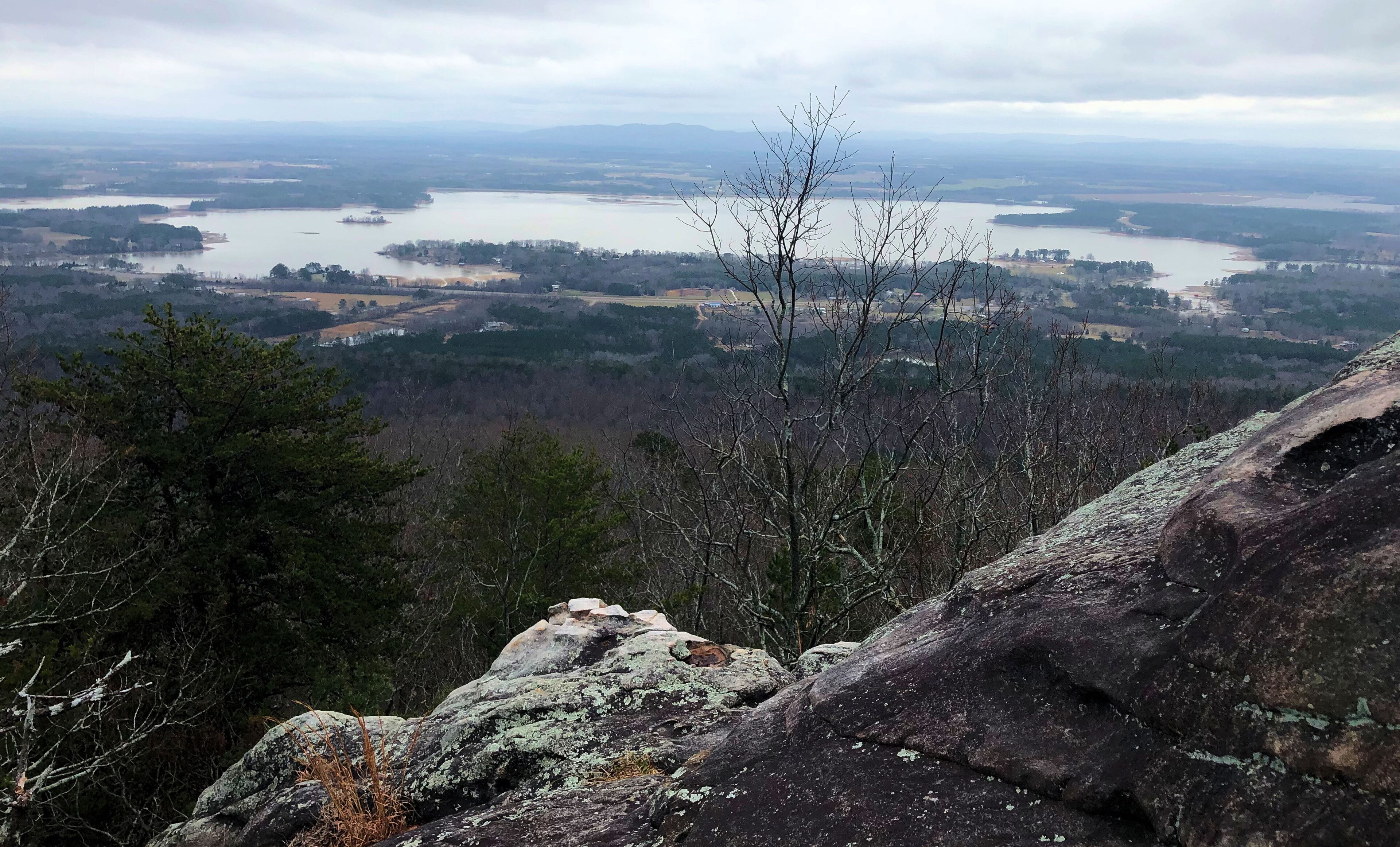 A mountainous landscape with a lake, forested areas, and rocky outcrops.