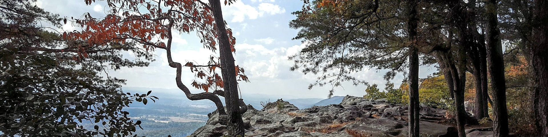 A rocky mountain landscape with autumn foliage and a distant view of the valley.