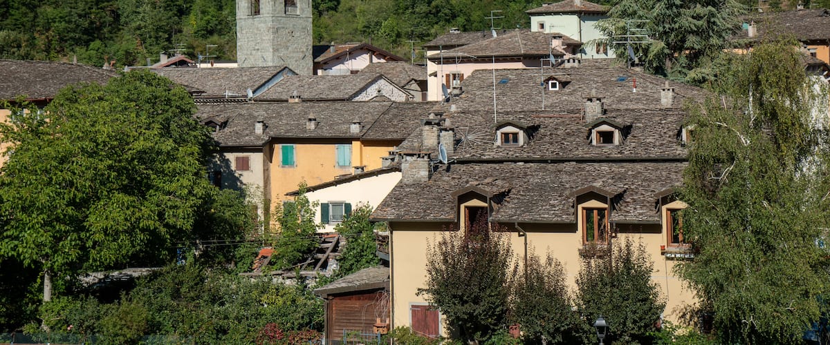 A village with stone buildings, a church with a green spire, and a forested hillside.