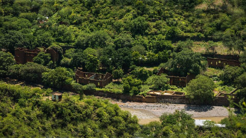 An aerial view of a lush, green landscape with scattered ruins and a river.