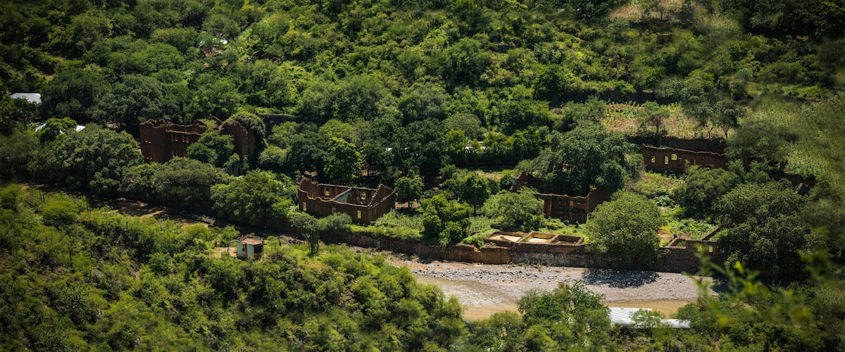 An aerial view of a lush, green landscape with scattered ruins and a river.