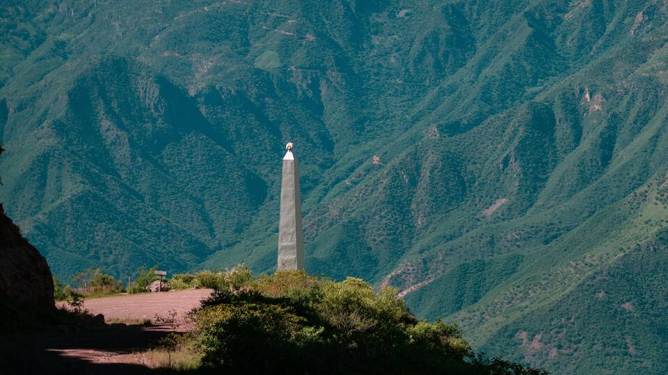 A tall monument in a mountainous area with dense green forests.